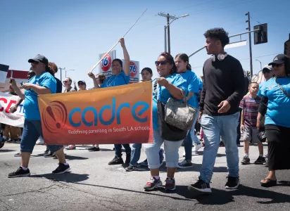 People are marching in the street holding a banner that says "CADRE"
