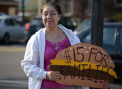 Woman with a white blouse and purple tee holding a sign.