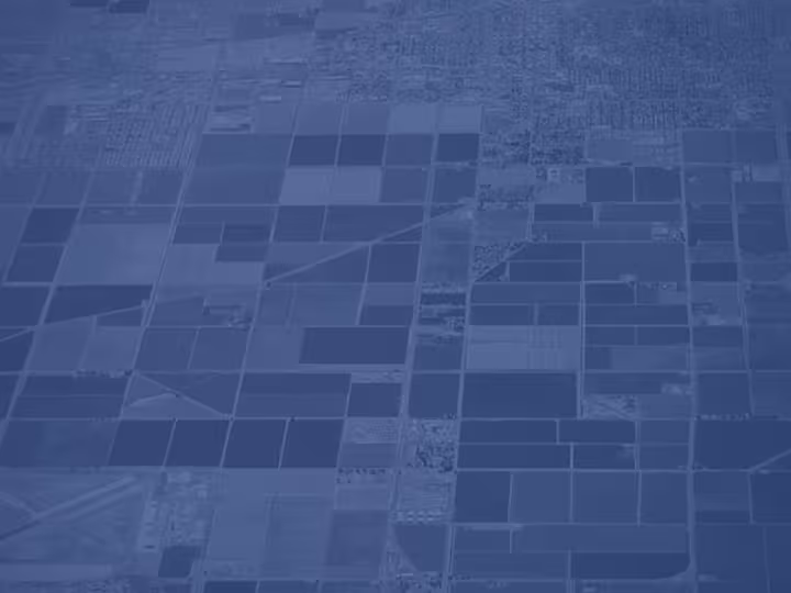 An aerial view of agricultural fields and urban areas, tinted in a monochromatic blue color.