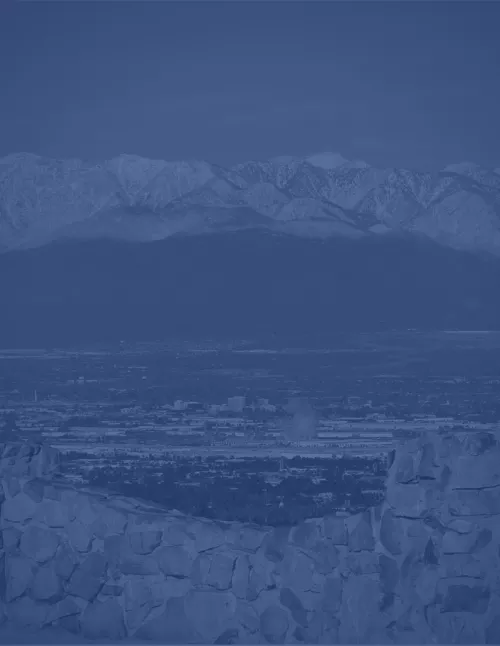 A monochromatic blue image showing a cityscape in a valley with mountains in the background and a stone wall in the foreground.