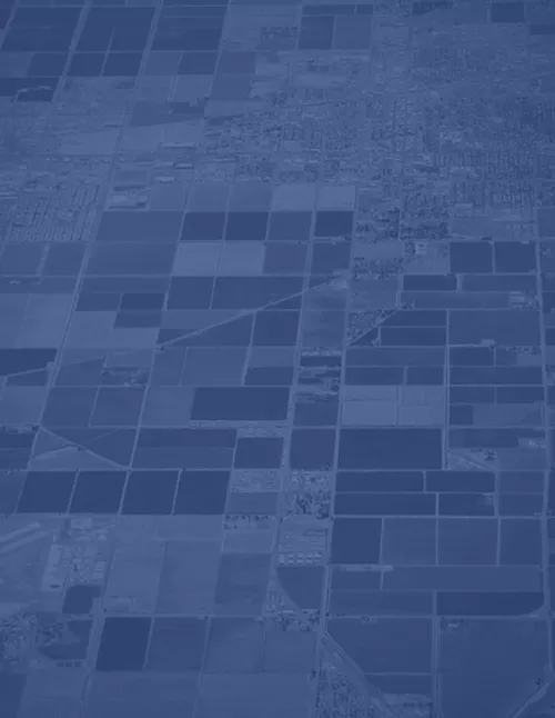 An aerial view of agricultural fields and urban areas, tinted in a monochromatic blue color.